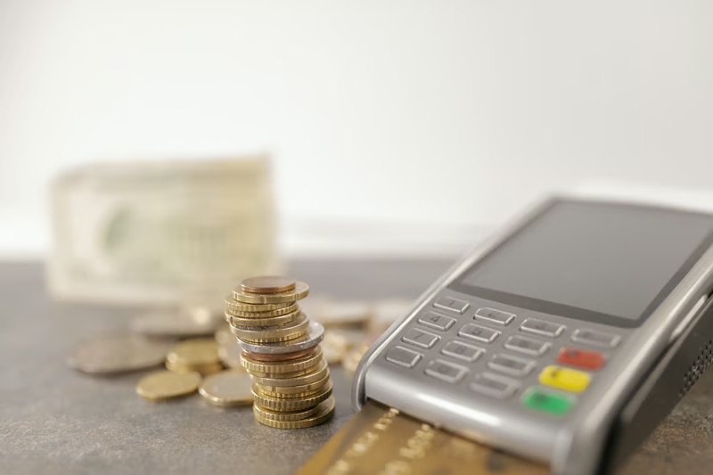 Coins, cash, credit card, and payment terminal representing the shift from traditional cash to cashless payments.