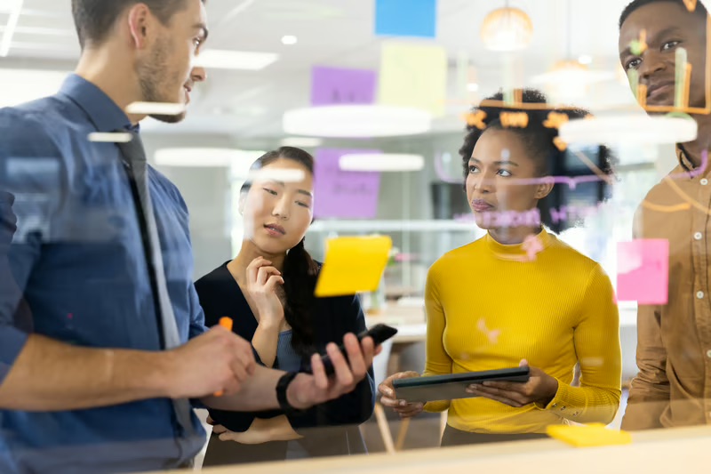 Business team using sticky notes and a tablet to identify customer experience problems and develop innovative solutions.